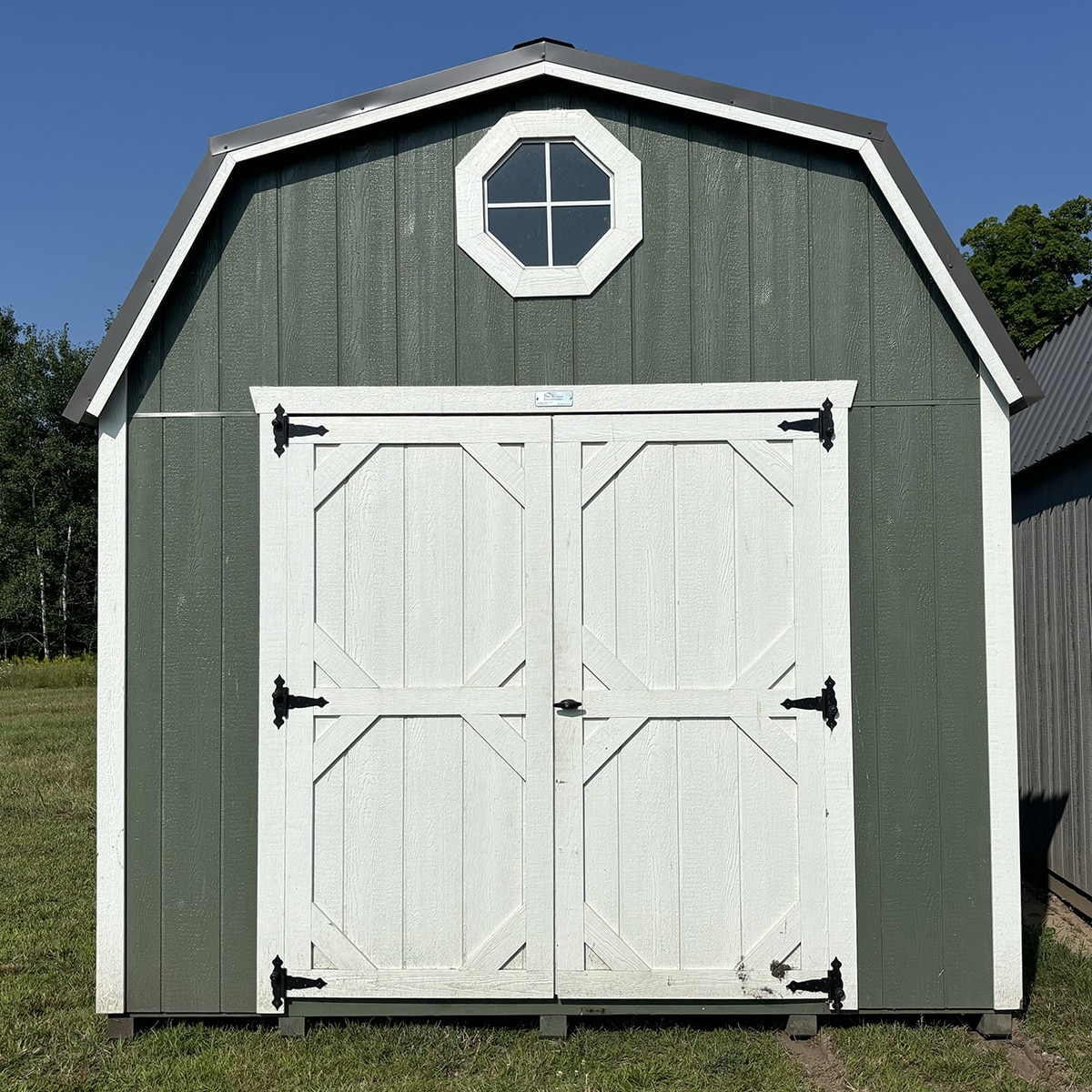 Pequea green lofted barn shed with white trim and white barn doors in a field on a sunny day.