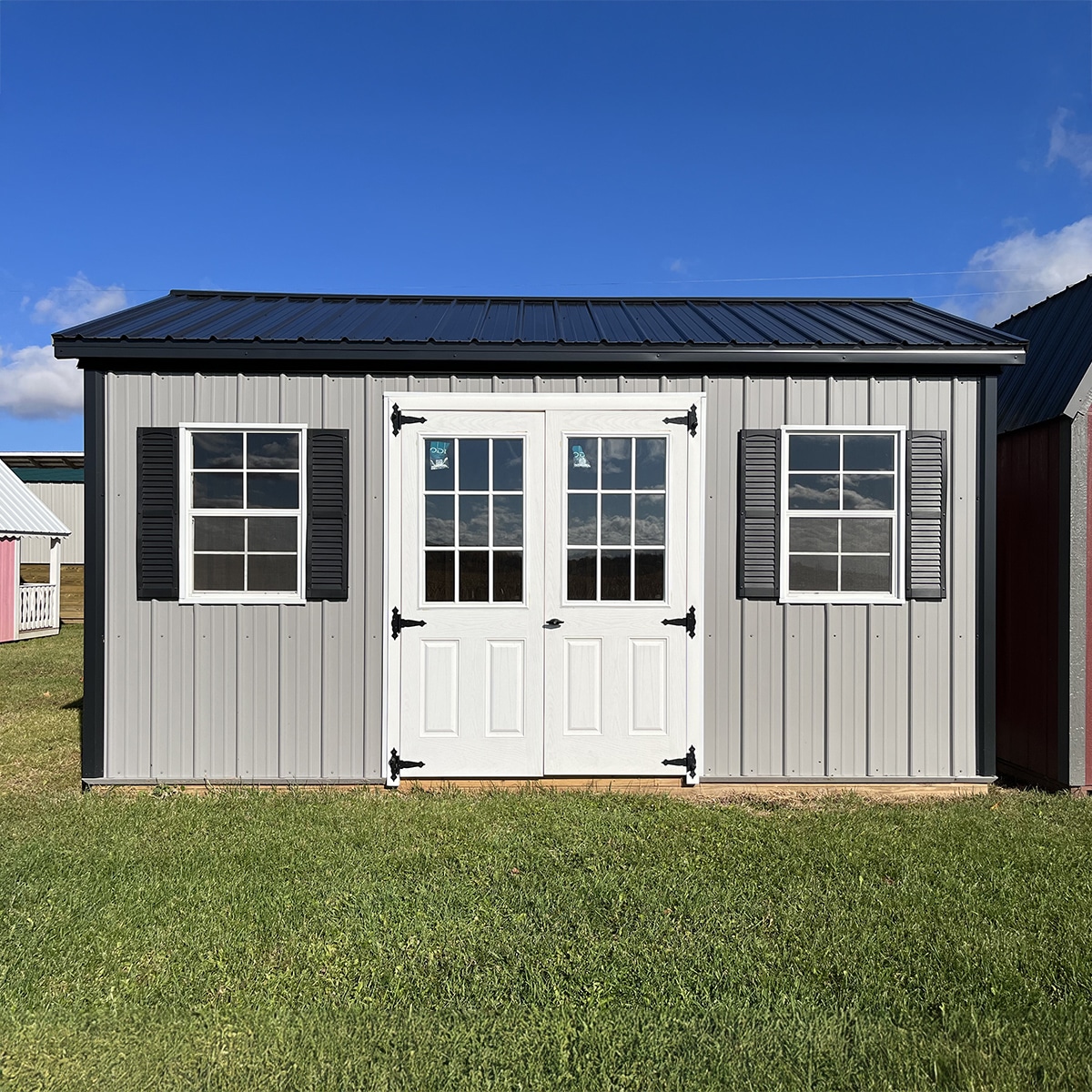 Gray metal gable garden shed with lots of windows and white double doors.