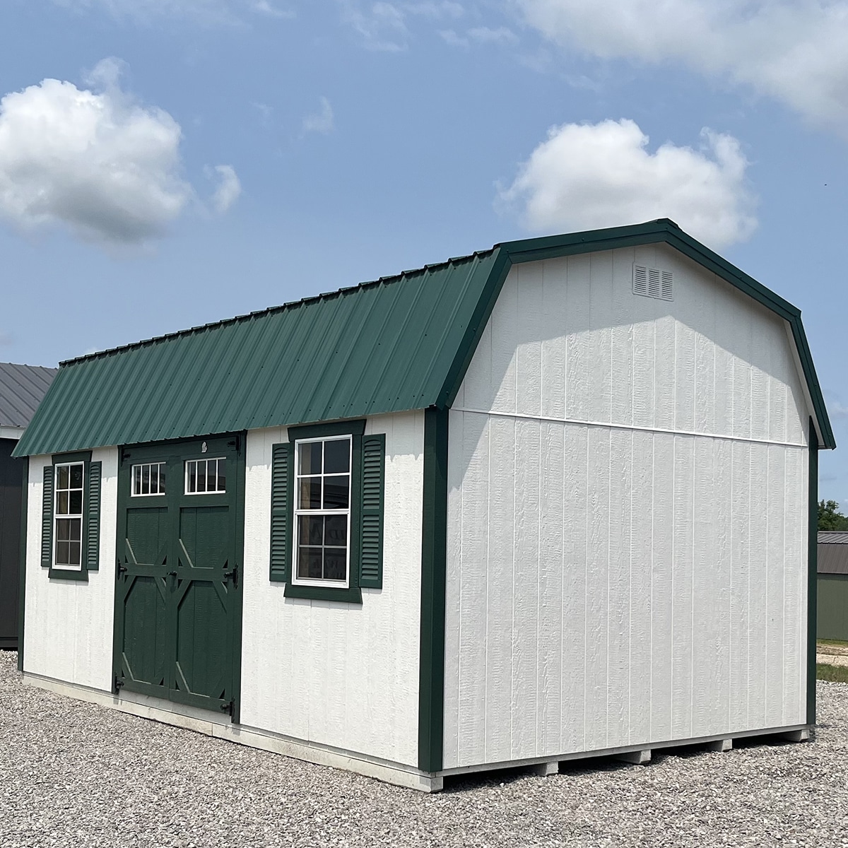 White lofted garden shed with green trim, metal roof, and green barn doors